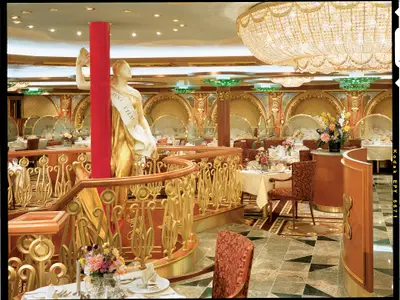 Opulentes Restaurant der Carnival Spirit. Goldene Statue 'Jena Eylau Wagram', gedeckte Tische, rote Stühle, Golddekor und Kristallleuchten.