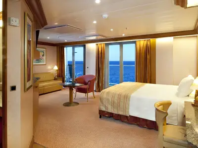 Helle und geräumige Suite auf der Carnival Spirit mit großem Bett, Sitzbereich, Schreibtisch und Glastüren zum Balkon mit Meerblick.