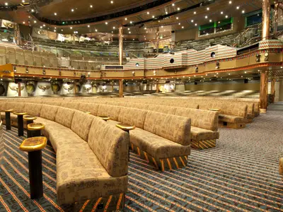 Großes, leeres Theater auf der Carnival Spirit. Ägyptisches Design mit goldenen Sitzbänken, gemustertem Teppich und verzierten Wänden. Stimmungsvolle Beleuchtung.