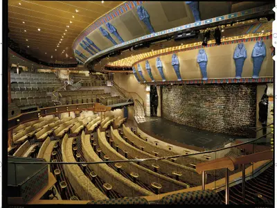 Ein großer Theatersaal auf der Carnival Spirit mit mehreren Sitzreihen, einer beleuchteten Bühne und ägyptischen Dekorelementen wie Sarkophagen und Hieroglyphenwänden.