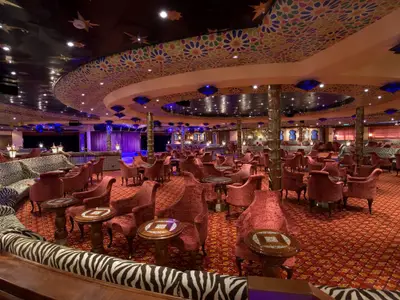 Eine luxuriöse, weitläufige Schiffs-Lounge im orientalischen Stil mit roten Teppichen, vielen roten Samtsesseln und Zebra-Sofas. Die Decke ist reich verziert und beleuchtet.