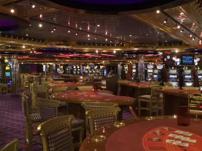 Ein geräumiges Casino auf der Carnival Splendor, ausgestattet mit zahlreichen hell beleuchteten Spielautomaten, roten Blackjack- und Roulette-Tischen sowie eleganten Stühlen, jedoch ohne Gäste.