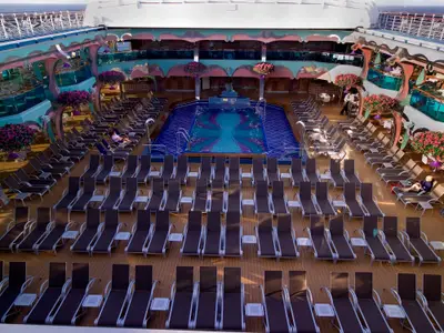Luftaufnahme eines farbenfrohen Pooldecks auf der Carnival Splendor mit blauem Pool, vielen Liegestühlen, Pflanzen und Decks auf mehreren Ebenen.