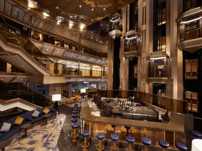 Ein luxuriöses Atrium der Carnival Sunrise, das sich über mehrere Decks erstreckt. Eine elegante Bar mit Barhockern ist im Vordergrund, flankiert von breiten Treppen und mehreren gläsernen Aufzügen.