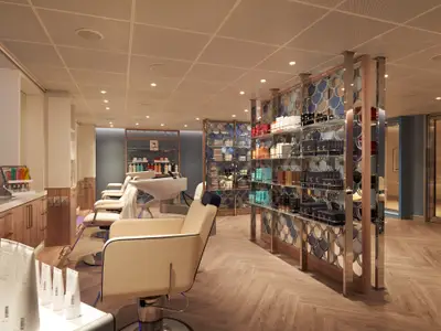 Innenansicht eines modernen Friseursalons auf der Carnival Sunrise. Mehrere cremefarbene Friseurstühle stehen vor Waschbecken. Links sind Holzschränke mit Ablagefläche, rechts hohe, spiegelnde Regale mit Pflegeprodukten. Der Boden ist ein hellbraunes Fischgrätparkett. Keine Personen sichtbar.