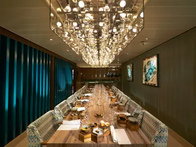 Ein langer, festlich gedeckter Esstisch in einem eleganten Spezialitätenrestaurant auf der Carnival Sunrise. Die Decke ziert eine beeindruckende Lichtinstallation aus Glas und Spiegeln.