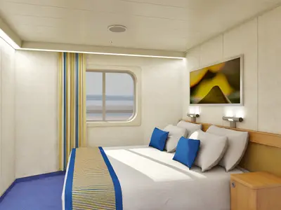 Eine moderne Außenkabine auf der Carnival Sunshine mit einem gemütlichen Doppelbett, blauen Kissen und einem Fenster, das einen Blick auf das Meer bietet. Eine gelb-blau gestreifte Tagesdecke und Gardinen setzen Farbakzente. An der Wand hängt ein abstraktes Kunstwerk. Der Raum ist hell beleuchtet, ohne Personen.
