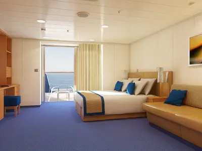 Helle Balkonkabine auf der Carnival Sunshine mit blauem Teppich, großem Doppelbett, Schreibtisch und einem Sofa. Durch die Glastür ist ein Balkon mit Meerblick sichtbar.