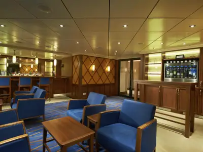 Geräumige, elegant beleuchtete Bar-Lounge auf der Carnival Sunshine. Blaue Sessel, Holztische und eine Bar mit Weindispenser füllen den Raum. Die Decke hat eingelassene Lichter.
