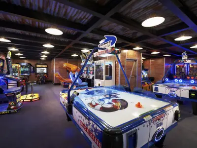 Ein lebhaftes Spielzimmer auf der Carnival Sunshine mit einer Reihe von Arcade-Automaten und mehreren Airhockey-Tischen. Die Wände sind aus Ziegeln und der Raum ist hell beleuchtet, was eine aufregende Atmosphäre schafft.