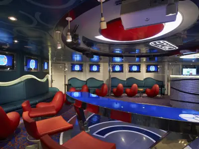 Helle, moderne Lounge an Bord der Carnival Sunshine mit blauer Theke, leuchtenden Akzenten und zahlreichen roten Sitzmöbeln. Mehrere Bildschirme zeigen das 'Circle C' Logo.
