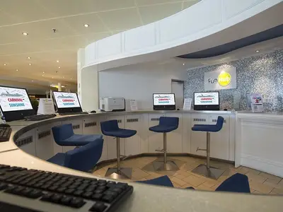 Eine gebogene Theke mit mehreren Computern und blauen Barhockern im 'Fun Hub' der Carnival Sunshine. Eine Wand ist mit kleinen glänzenden Fliesen verziert, darüber ein 'Fun Hub'-Schild.
