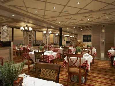 Innenansicht eines italienisch anmutenden Spezialitaetenrestaurants mit vielen gedeckten Tischen, rot-weiß karierten Tischdecken und holzvertäfelten Wänden und Decke. Große Fensterfronten bieten eine Abendstimmung.