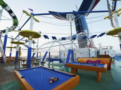 Oberes Deck der Carnival Sunshine mit blauen Billardtischen, Foosball, Seilgarten und Wasserrutsche. Der bunte Schornstein ist im Hintergrund zu sehen.