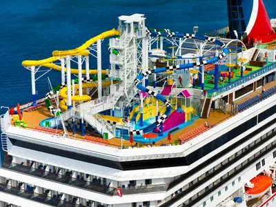 Aquapark auf der Carnival Sunshine: bunte Wasserrutschen in Gelb, Blau, Grün, Planschbereiche. Das blaue Meer umgibt das Deck.