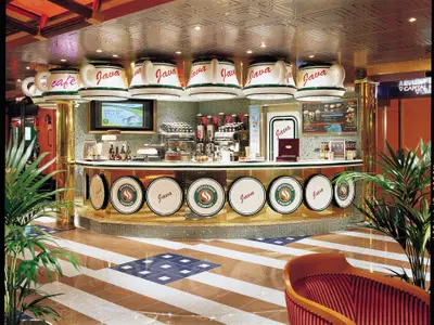 Ein stilvolles Kaffee auf der Carnival Valor mit einer langen Theke und großen, umgedrehten Kaffeetassen als Lampenschirme. Die Theke ist mit Desserts und Kaffeezubereitungsgeräten bestueckt. Der Boden hat ein auffaelliges Muster.
