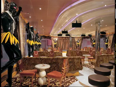 Eine exzentrisch dekorierte Bar mit glänzenden schwarzen Statuen in gelben Bananenröcken und Perlenketten. Die Bar hat Zebra-Muster-Sitzmöbel, eine Bühne mit braunen Vorhängen und moderne Deckenbeleuchtung.