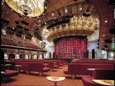 Das große Theater der Carnival Valor, stilisiert als mittelalterliche Burg. Eine Bühne mit einem bunten, roten Vorhang ist von roten Sitzreihen umgeben. Die Decke ist reich verziert, und an den Wänden sind Burgenelemente zu sehen.