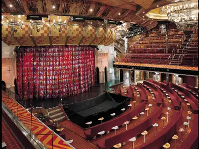 Ein prunkvolles Theater der Carnival Valor im mittelalterlichen Design mit einer Bühne, rotem Vorhang voller Wappen und aufsteigenden roten Sitzreihen.