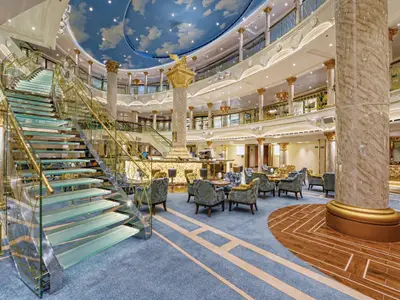 Luxuriöses Atrium der Carnival Venezia mit goldener Glas-Wendeltreppe, beleuchteter Bar und Sitzgruppen. Himmels-Deckengemälde. Marmorsäulen und Goldakzente prägen das elegante Ambiente.