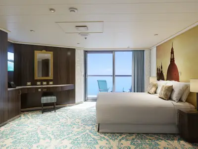 Elegante Balkonkabine mit Doppelbett, Schreibtisch, Spiegel und Zugang zum Balkon mit Meerblick. Die Wand über dem Bett zeigt eine goldene Stadtlandschaft.