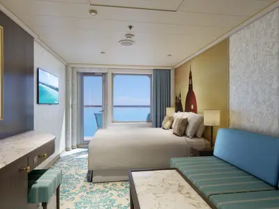 Blick in eine moderne Balkonkabine auf der Carnival Venezia. Zu sehen sind ein Doppelbett, ein Sofa, ein Flachbildschirm und ein Balkon mit weitem Meerblick.