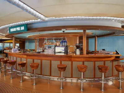 Eine elegant gestaltete, runde Poolbar aus Holz mit vielen Barhockern und einer gut bestückten Bar. Im Hintergrund ist durch große Fenster das weite Meer zu sehen.