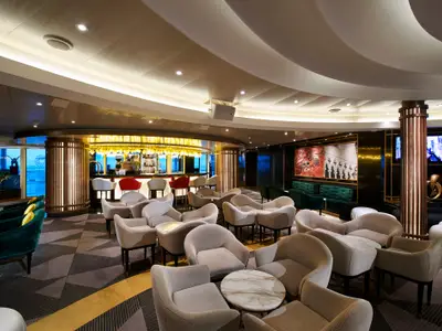 Ein elegantes Schiffs-Interieur mit einer Bar im Hintergrund, vielen hellen Loungesesseln und grünen Sofas. Die Decke hat eine geschwungene Form mit eingelassenen Lichtern. Große Fenster auf der linken Seite bieten einen Blick nach draußen.