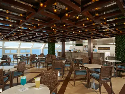 Helle Bar-Lounge auf der Carnival Venezia mit zahlreichen Tischen, Stühlen, einer Bar und großen Fenstern mit Meerblick. Die Decke ist mit Holzbalken und Lichterketten gestaltet.
