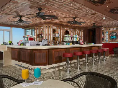 Eine moderne Bar auf der Carnival Venezia mit einer U-förmigen Theke, roten Lederhockern und einem auffälligen Decken- und Wanddesign im orientalischen Stil. Große Fenster bieten Meerblick.