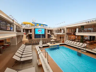 Das weitläufige Pooldeck der Carnival Venezia mit Pool, Liegestühlen, DIVE-IN Movies-Leinwand und umgebenden Restaurants. Im Hintergrund sind Wasserrutschen zu sehen.