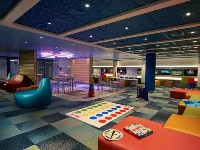 Heller, bunter Entertainment-Bereich auf der Carnival Venezia mit Twister-Matte, Connect 4, Videospielkonsolen und bequemen Sitzgelegenheiten.