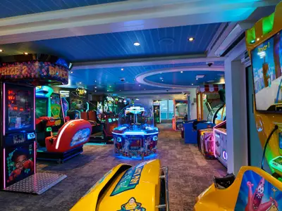 Ein lebhafter Innenbereich der Carnival Venezia, gefüllt mit bunten Arcade-Spielen und leuchtenden Automaten. Der Boden ist mit Teppich ausgelegt und die Decke hat blaue Akzente mit Lichtern. Mehrere Spielautomaten sind sichtbar, darunter ein Boxautomat und Fahrsimulatoren.