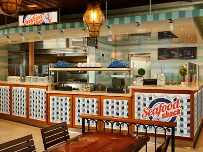 Eine helle und moderne Seafood Shack Buffettheke auf der Carnival Venezia mit hellgrünen Fliesen, Holzverkleidung und maritimen Dekorationen. Das Schild "Seafood Shack" ist deutlich zu sehen.