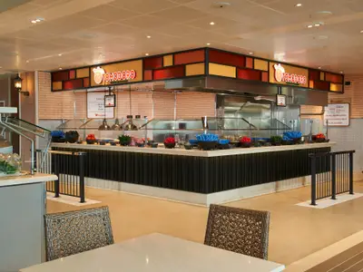 Blick in das helle, moderne Buffetrestaurant Tomodoro mit Theke voller Zutaten für Tacos und Burritos. Orange und rote Akzente, helle Backsteinwand.