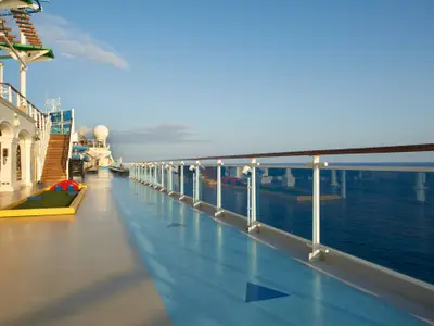 Sonniges Oberdeck der Carnival Venezia mit Mini-Golfplatz, blauer Joggingbahn und Glasgeländer. Weite des Ozeans und blauer Himmel sichtbar.