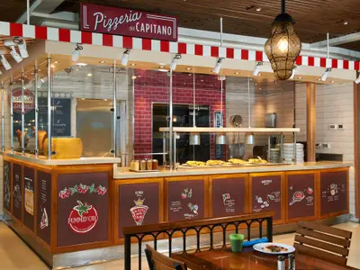 Pizzatheke im 'Pizza del Capitano' Restaurant an Bord. Ausgestellte Pizzen, ein Kaeserad und Gewuerze sind sichtbar. Rote Ziegelwände und Pizzaoefen im Hintergrund.