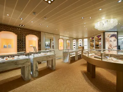 Eine luxuriöse Bulgari Boutique an Bord der Carnival Venezia. Verschiedene Schmuckstücke und Accessoires sind in Vitrinen ausgestellt, mit Gold- und Marmorakzenten und einer glitzernden Deckenlampe.