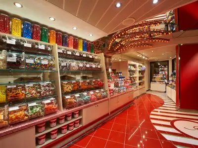 Heller Süßwarenladen auf der Carnival Venezia mit Regalen voller bunter Bonbons und Schokolade in Spendern. Roter Boden mit gestreiften Mustern, beleuchtete Deckeninstallation.