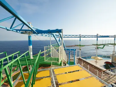 Weitwinkelaufnahme eines Oberdecks der Carnival Venezia mit blauem Hochseilgarten, grünem Minigolfbereich und einem Pool. Das Meer ist im Hintergrund sichtbar unter einem klaren Himmel.