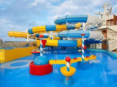 Ansicht eines farbenfrohen Wasserparks auf der Carnival Venezia. Mehrere gelbe und blaue Wasserrutschen schlängeln sich über einen blauen Boden mit Wasserspielen.