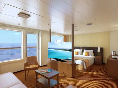 Einladende Suite der Carnival Vista mit Doppelbett, Sitzbereich und großen Fenstern zum Ozean. Ein Fernseher zeigt eine tropische Insel. Helle, moderne Einrichtung.