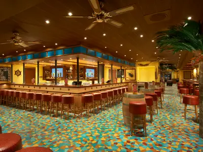 Helle Bar auf der Carnival Vista mit langem Holztresen, roten Hockern und buntem Mosaikboden. Holzdecke, Ventilatoren und künstliche Palmen schaffen tropisches Flair. Keine Personen.