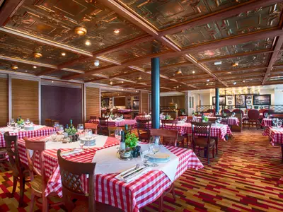 Geräumiges, festlich gedecktes Restaurant auf der Carnival Vista. Die Tische sind mit rot-weiß karierten Tischdecken, Gläsern und Geschirr ausgestattet. Die Decke ist mit kupferfarbenen Kassetten und Holzbalken verziert. Der Teppich hat ein modernes geometrisches Muster in Rot- und Brauntönen. Keine Personen sind sichtbar.