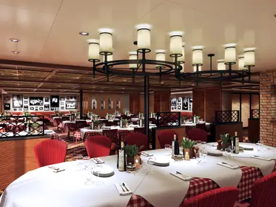 Innenansicht eines italienischen Spezialitätenrestaurants auf der Carnival Vista. Mehrere Tische mit rot-weiß karierten Tischdecken, roten Stühlen und Kronleuchtern unter einer verzierten Decke. Die Wände sind mit Ziegeln und Schwarz-Weiß-Fotos dekoriert. Eine gemütliche und einladende Atmosphäre für ein Abendessen.