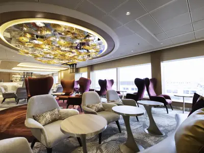 Lounge auf dem Kreuzfahrtschiff Celebrity Apex mit opulentem Deckenleuchter. Moderne Sessel und Tische sind in Gruppen arrangiert. Große Fenster bieten einen Panoramablick.