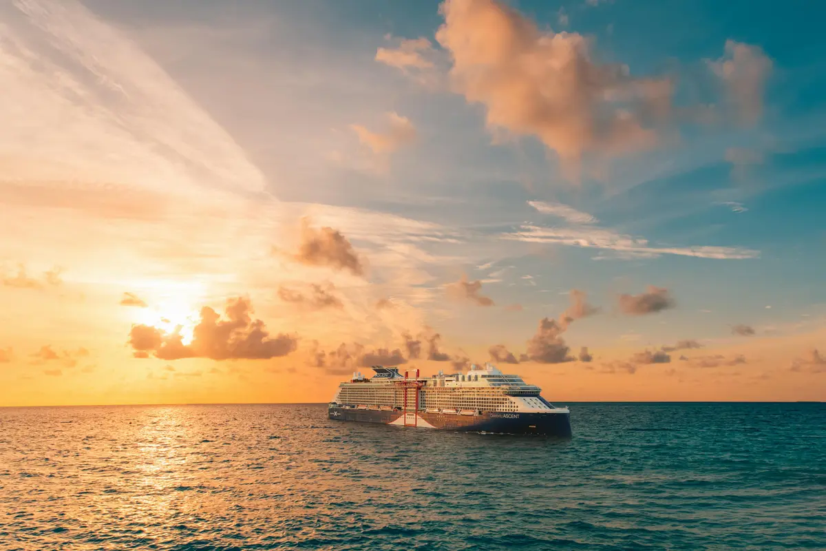 Das Kreuzfahrtschiff Celebrity Ascent fährt auf dem offenen Meer. Die Abendsonne taucht Himmel und Wasser in warme Orange- und Blautöne.