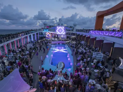 Abendliche Feier auf dem Pooldeck der Celebrity Ascent mit vielen Gästen. Im Zentrum ein beleuchteter Pool und eine Bühne. Eine glänzende Oktopus-Skulptur fällt auf. Meer im Hintergrund.