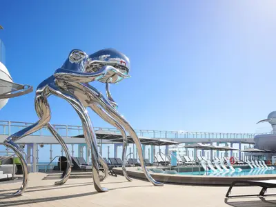 Große, glänzende Oktopus-Skulptur auf dem sonnigen Pooldeck der Celebrity Ascent. Im Hintergrund ein Pool, Liegestühle und Schirme unter blauem Himmel.