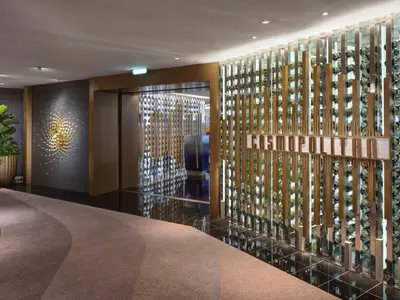 Blick in den eleganten Eingangsbereich des Restaurants "Cosmopolitan" mit einer Weinflaschenwand und einem goldenen Wandkunstwerk. Ein grosser Pflanzentopf steht links.